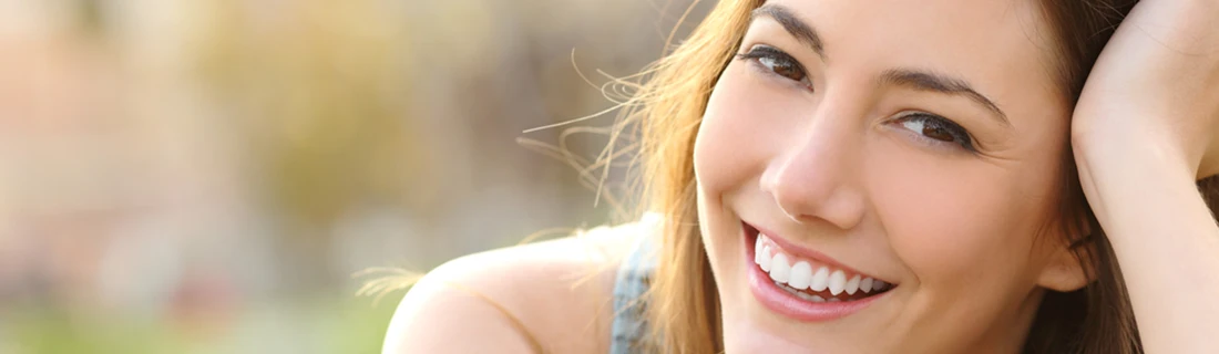 A smiling woman who's expression is engaging with light brown hair and eyes shows her bright, white teeth in a close-up.